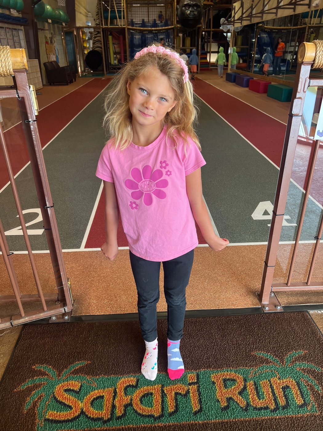 A smiling girl standing on a padded platform inside the Safari Run play structure