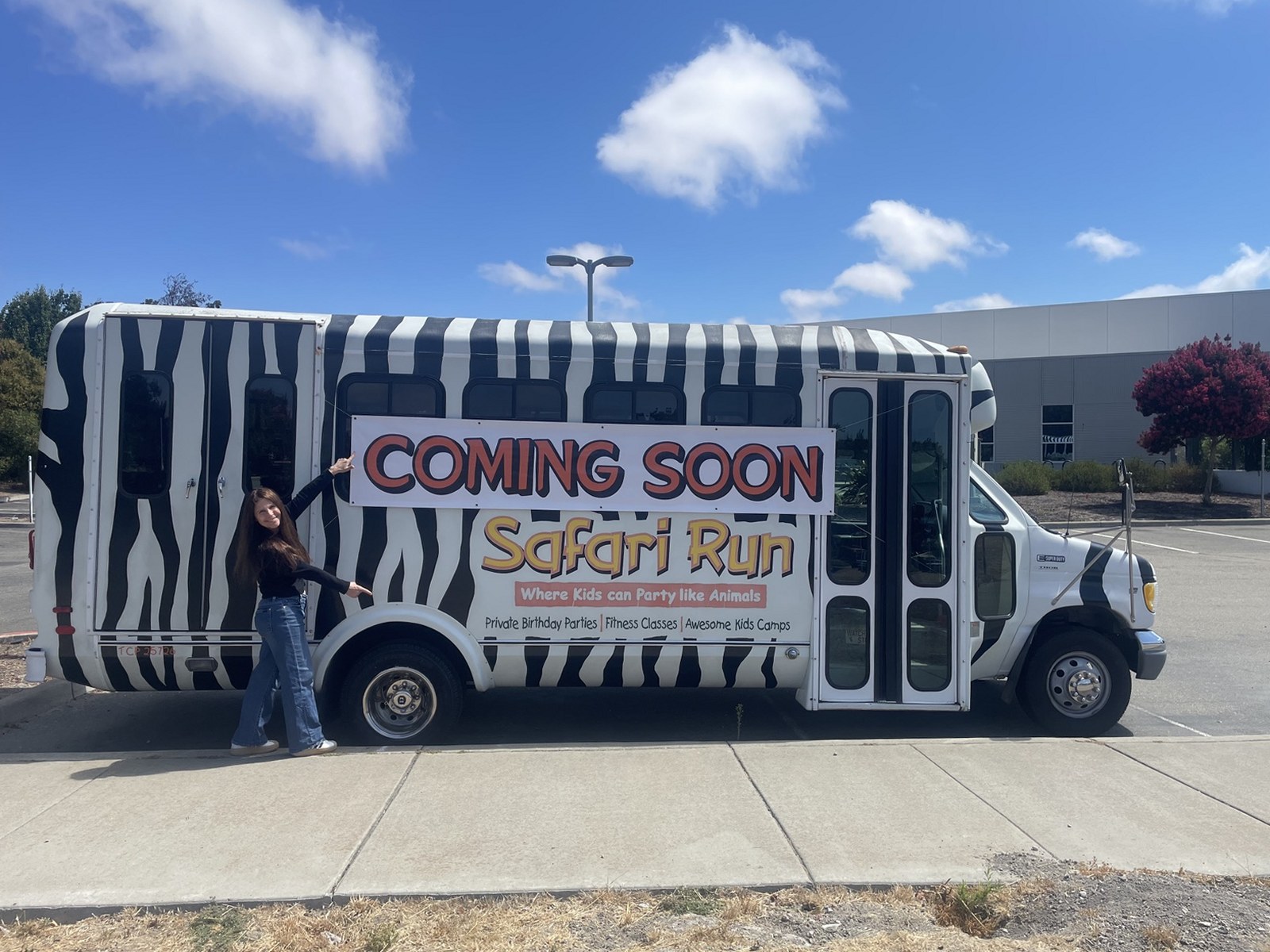 The Safari Run zebra-striped bus parked outside the Livermore site, with a Coming Soon banner along its side