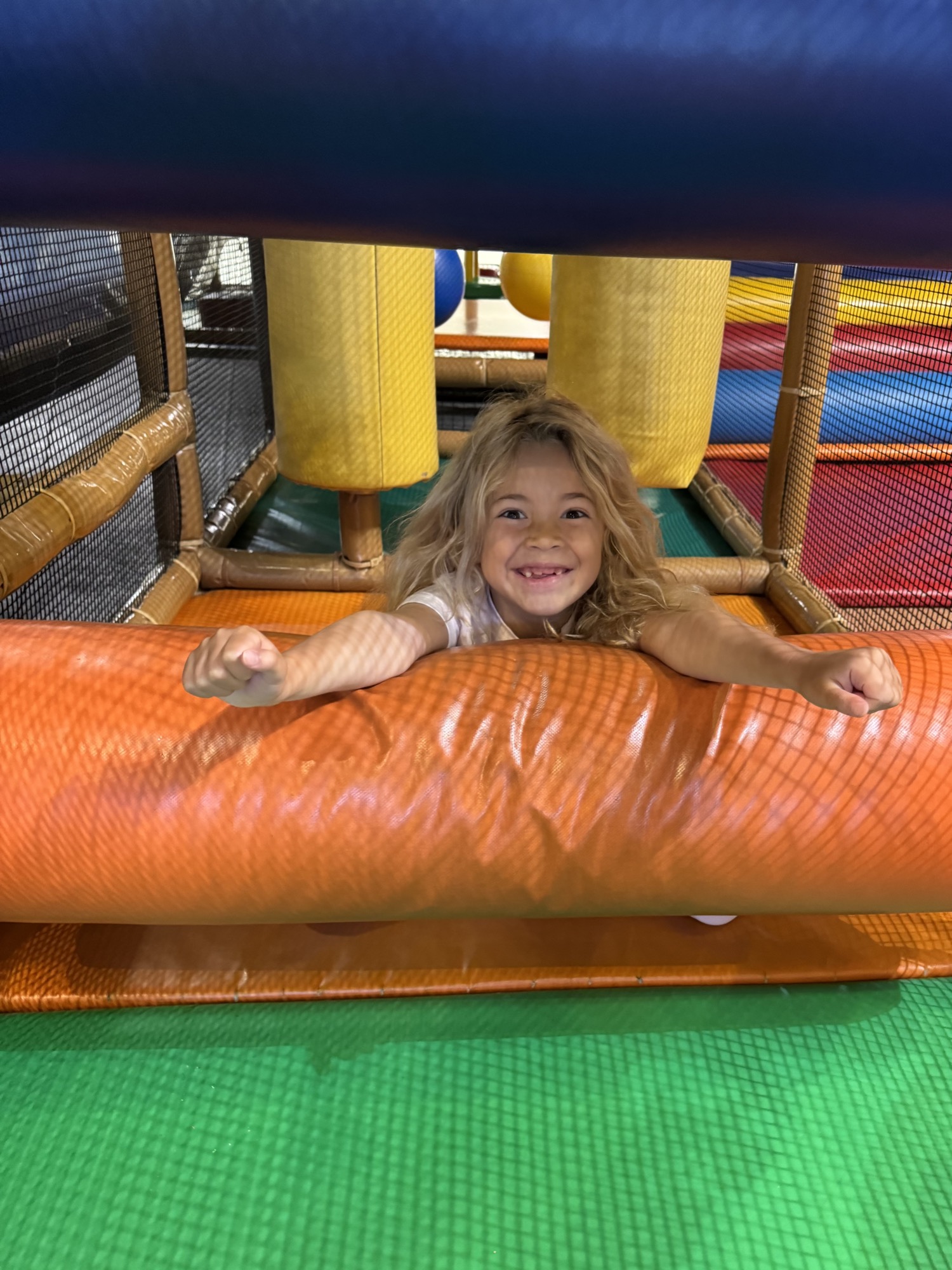 A smiling girl leaning over an orange padded roller inside the Safari Run play structure